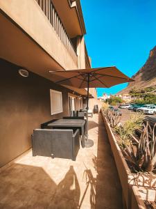 eine Terrasse mit Tischen und einem Sonnenschirm an der Seite eines Gebäudes in der Unterkunft Playa Maria Appartment 14 (Vista del Valle) in Valle Gran Rey