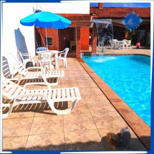 a pool with chairs and an umbrella and a table and chairs at Hostel&Pousada Equilíbrio in Praia Grande