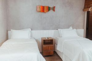 - 2 lits avec des draps blancs et une table de chevet dans l'établissement Triplex Temporada Areia e Mar Patacho - Casa Verde, à Porto de Pedras