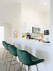 a kitchen with a counter with four green chairs at Luxury Modern Pool House close to theme parks. in Kissimmee
