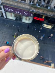 a hand holding a cup with a view of a city at Knez Mihailova Apartman in Belgrade
