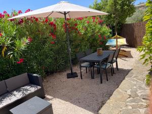 a table and chairs under an umbrella in a garden at Bas de villa indépendant avec espace jacuzzi privé in Le Lavandou