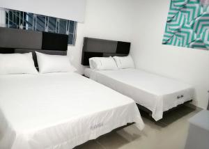 two beds in a hotel room with white sheets at Plaza Real Edificio Turístico in Melgar