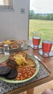 un tavolo con un piatto di prodotti per la colazione e due bicchieri di vino di Under the Stars Shepherds Huts at Harbors Lake a Newchurch