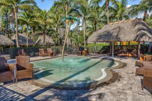 a pool with a straw umbrella and chairs and palm trees at Yuba Oasis in Lely Resort