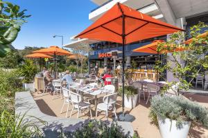 un restaurante con mesas y sillas con sombrillas naranjas en Oceanus Bokarina Beach, en Kawana Waters