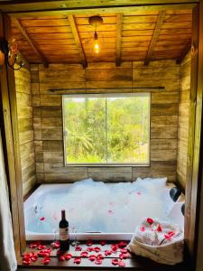 a bath tub with a bottle of wine and a window at Chalé Recanto dos Pinheiros in Monte Verde