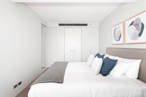 a white bedroom with a large bed with blue pillows at DH707 - 1 bedroom unit Victoria St - Darlinghurst in Sydney