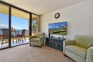 a living room with a tv and chairs and a balcony at Maalaea Banyans 203 in Wailuku