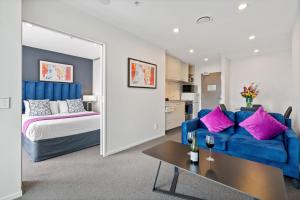 a living room with a blue couch and a bed at Proximity Apartments Manukau / Auckland Airport in Auckland