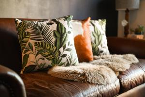 a brown leather couch with pillows and a cat on it at Eclectic Heritage Paradise Simon's Town in Simonʼs Town