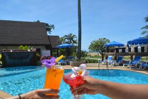 a person holding a drink in front of a pool at Lanta IL Mare Beach Resort in Ko Lanta