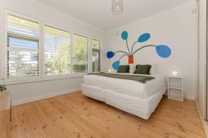 a white bedroom with a large bed and windows at Belle Escapes - Beauty at the Beach in Glenelg