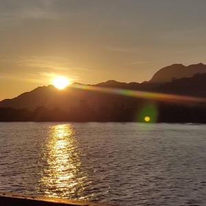 un coucher de soleil sur une étendue d'eau avec des montagnes en arrière-plan dans l'établissement the sunset view lagoon suite, à Pantai Cenang