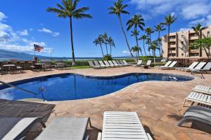 a swimming pool with lounge chairs and palm trees at Island Sands 210 in Maalaea