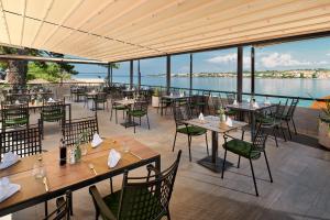 een restaurant met tafels en stoelen en uitzicht op het water bij Hotel Pinija in Petrcane