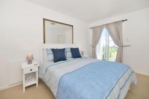 a white bedroom with a blue bed and a window at 25 The Tides in Struisbaai