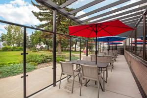 um pátio com uma mesa e cadeiras e um guarda-sol vermelho em Best Western PLUS Port O'Call Hotel em Calgary