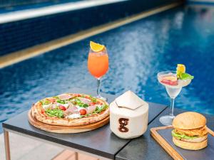 a table with a pizza and a drink next to a pool at Pullman Bangkok Hotel G in Bangkok