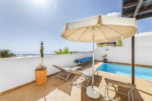 um pátio com um guarda-sol e cadeiras e uma piscina em Villa 6 - Villasexperience em Tías