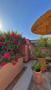 un balcón con flores rosas, una mesa y una sombrilla en Riad Dar Zaman en Marrakech