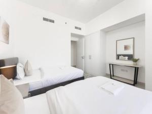 a white bedroom with two beds and a table at StoneTree - Spacious 3 BR in The Pulse C2 in Dubai