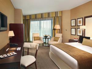 a hotel room with a bed and a desk and chairs at Mövenpick Grand Al Bustan in Dubai