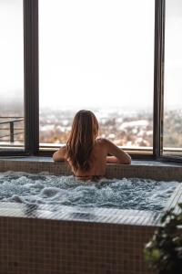 a woman sitting in a bath tub looking out a window at L'Ermitage Hôtel Cuisine-À-Manger in Saint-Cyr-au-Mont-dʼOr