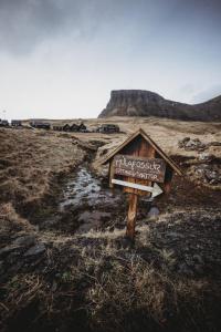 a sign in a field with a mountain in the background at Múlafossur Cottages by famous waterfall in Gásadalur in Gásadalur