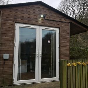 a large wooden shed with doors and a fence at Ogdenclough fisherie log cabin in Rochdale