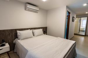 a bedroom with a large white bed and a nightstand at Hotel Mais1 in Campina Grande