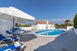 a group of chairs and a swimming pool with an umbrella at Casa Pachorrenta in Carvoeiro