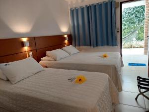 two beds in a hotel room with two yellow flowers on them at Pousada Lua Azul in Porto De Galinhas