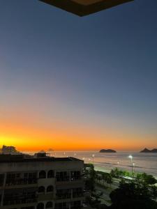 um pôr-do-sol sobre o oceano com um edifício e o oceano em Vista para o mar Barra da tijuca no Rio de Janeiro