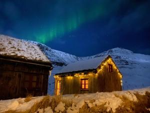 an aurora lights up the sky over a cabin at Múlafossur Cottages by famous waterfall in Gásadalur in Gásadalur