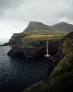 a waterfall on a cliff next to the ocean at Múlafossur Cottages by famous waterfall in Gásadalur in Gásadalur