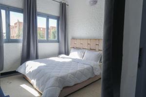 a bedroom with a bed with white sheets and windows at Hotel Warda in Ouarzazate