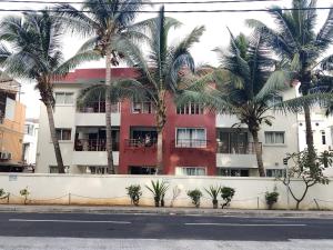 a red building with palm trees in front of it at Ashiana OceanSide Apartment in Flic-en-Flac