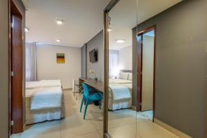 a room with two beds and a desk and a mirror at Hotel Mais1 in Campina Grande