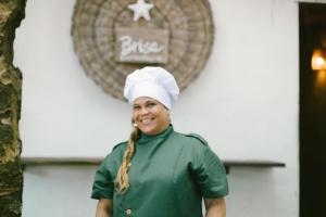 una mujer con un sombrero de cocinero parado frente a un cartel en Ventos Morere Hotel & Beach Club en Ilha de Boipeba