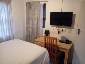 1 dormitorio con 1 cama y escritorio con TV en Tshidiso Guesthouse, en Centurion