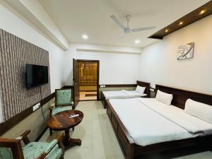 Habitación con 2 camas, mesa y TV. en Hotel Tirth by Sonu's, en Ujjain