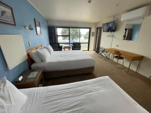 a hotel room with two beds and a desk at Bay Sands Seafront Studios in Paihia