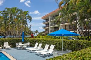 eine Terrasse mit Stühlen und einem Sonnenschirm neben einem Pool in der Unterkunft Maui Parkshore 312 - MCH in Kihei