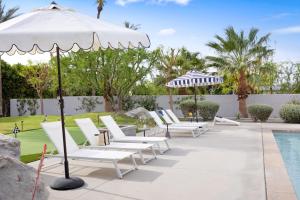 a row of lounge chairs under an umbrella next to a pool at Polo Villa 10 by AvantStay Backyard Oasis w Putting Green 260-320 6 Bedrooms in La Quinta