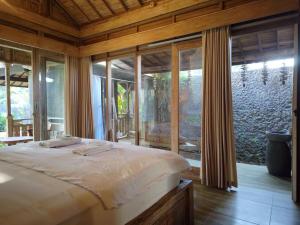a bedroom with a bed in a room with windows at Tangkas wooden house in Tampaksiring