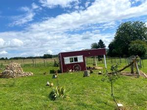 a small red shed in a field with chickens in the grass at Roulotte de Charme 