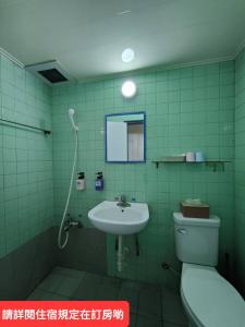 uma casa de banho com azulejos verdes, um WC e um lavatório. em Lu Zhou Hotel em Pingtung