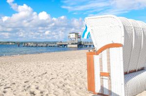 een witte stoel op een strand met een pier bij Ferienwohnung Ankerplatz 54 Nord in Glücksburg