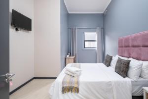 um quarto com uma grande cama branca e uma cabeceira rosa em Cape palm royal guest house em Cidade do Cabo